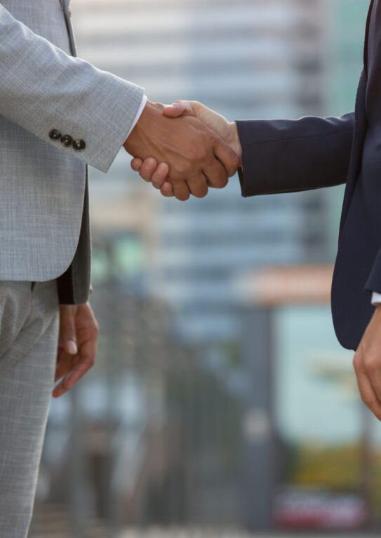 Businesspeople standing in city street and shaking hands. Business man and woman in office suits meeting outside. Successful partnership concept